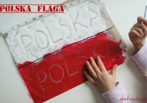 Dziecko odwzorowywuje napis Polska za pomocą patyczka